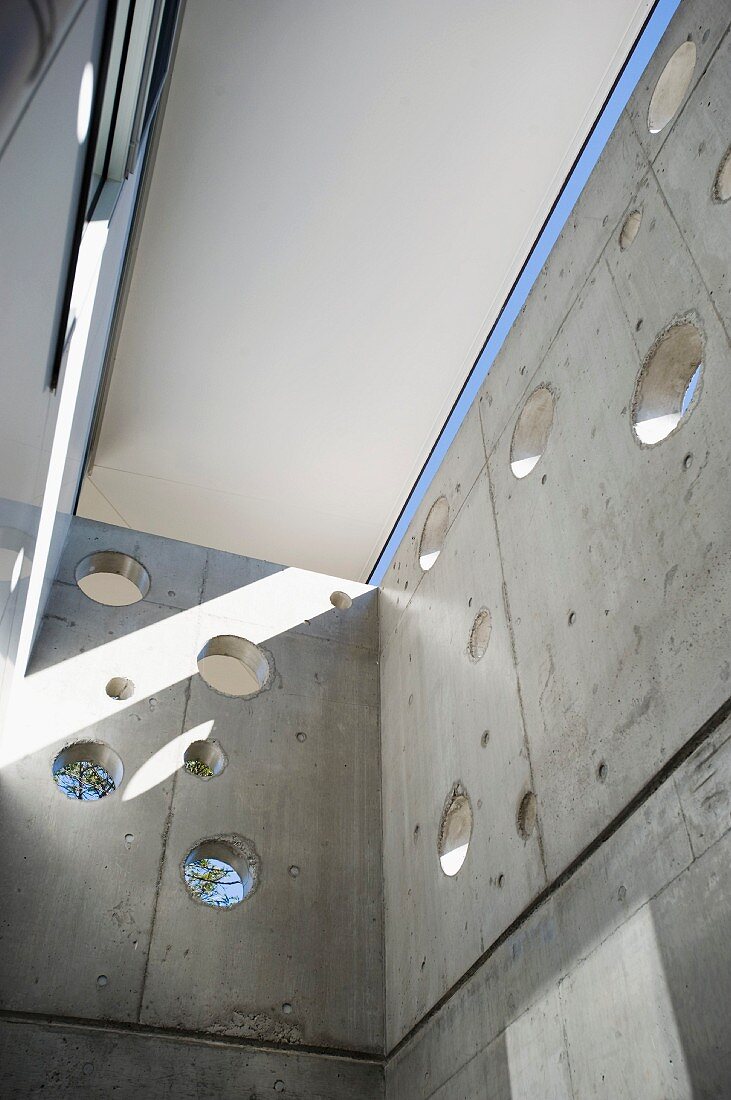 Light and shadow play in a shaft with circular holes in an exposed concrete wall
