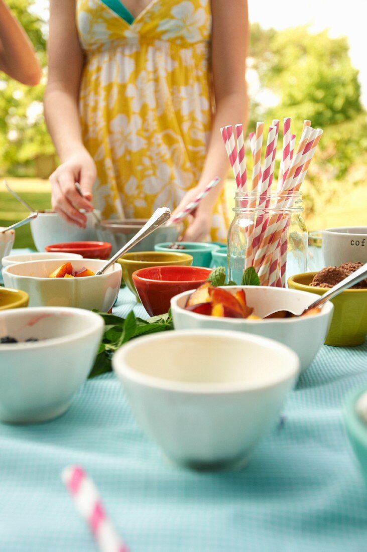 Table Set Up Outside with Bowls of Ice Cream and Toppings; Straws