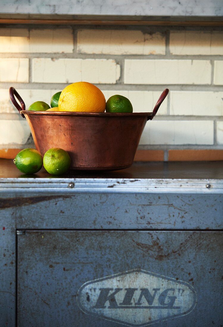 Oranges and Limes in a Copper Pot on a Counter