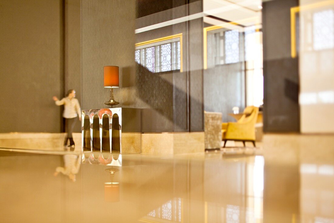 Grossräumiges minimalistisches Hotelfoyer mit glänzendem Boden und Frau im Hintergrund