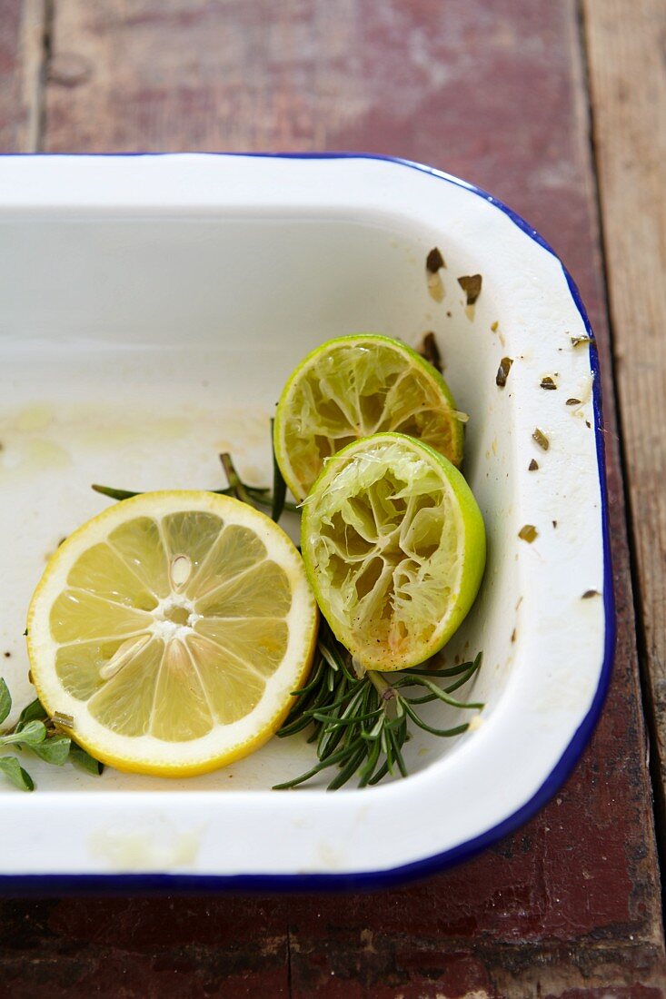 Lemon slices, squeezed limes and rosemary in a roasting tin