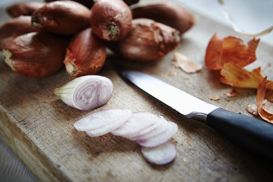 Whole and sliced shallots on a wooden board