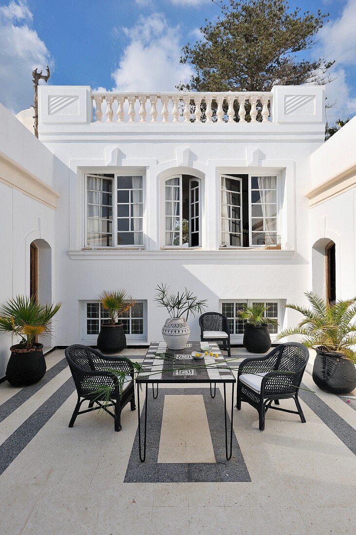 North African style courtyard with black and white theme with wicker chairs around a mosaic table and potted palms