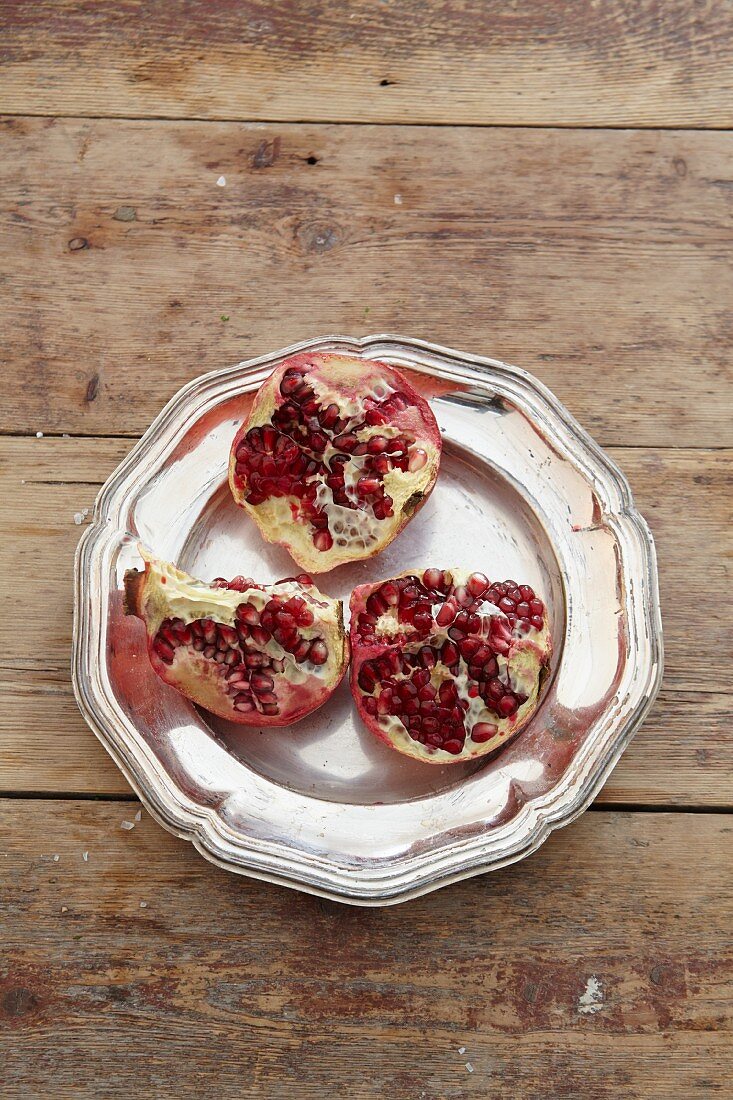 A pomegranate, sliced open, on a metal plate