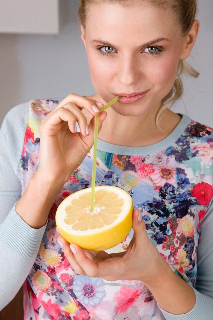A woman drinking from a grapefruit with a straw