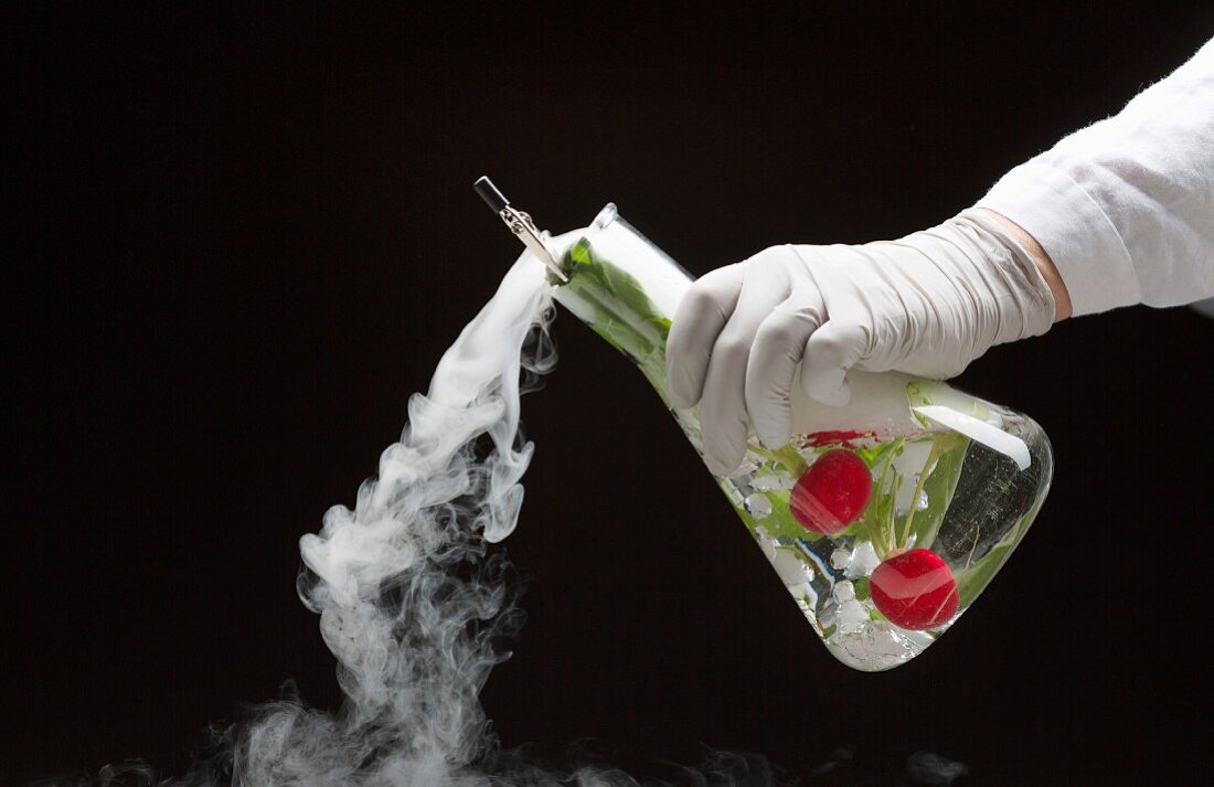 A hand holding a chemistry flask filled with radishes and dry ice