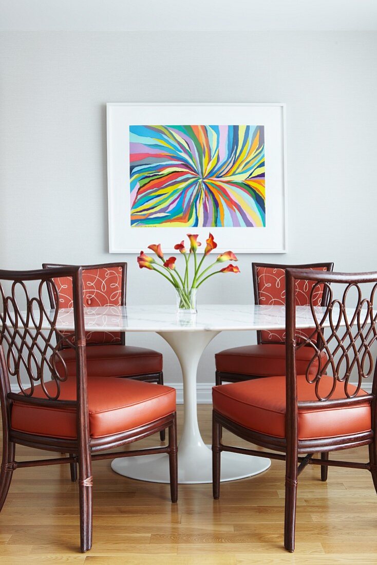 Classic table with marble top and wooden chairs with red leather seat cushions in front of modern artwork on wall