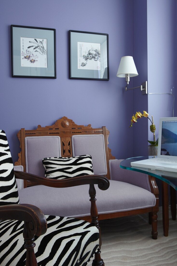 Armchair with zebra-pattern upholstery in front of antique armchair against lilac wall