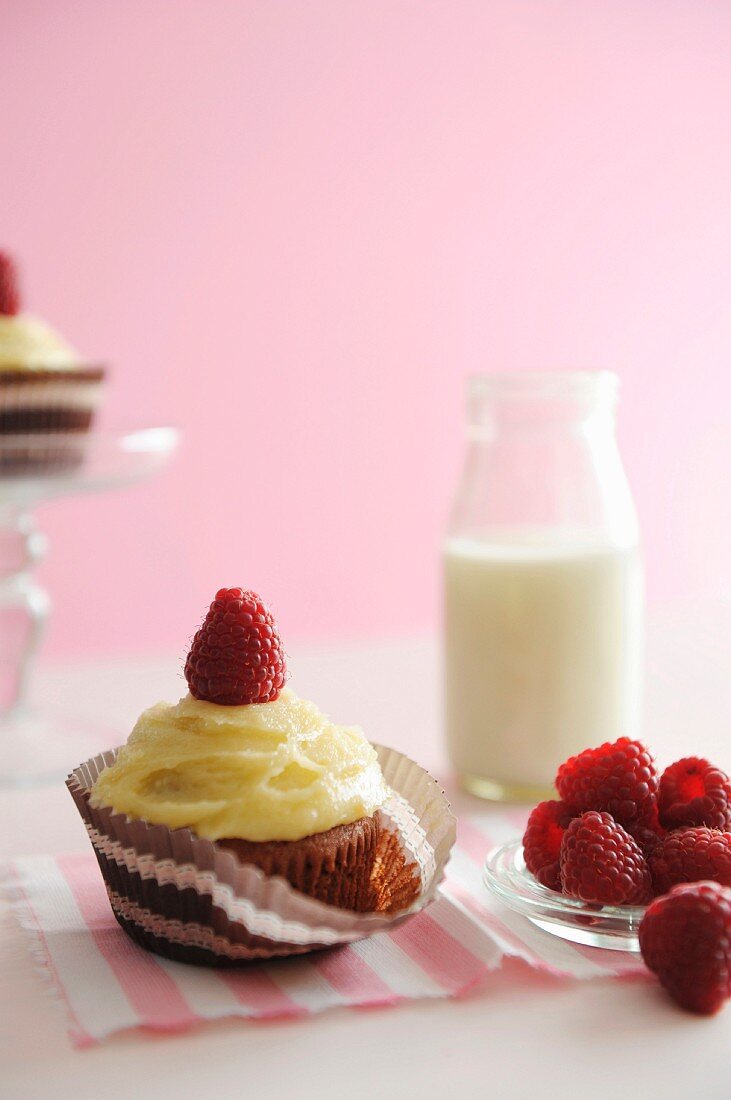 A raspberry cupcake with fresh raspberries and a bottle of milk