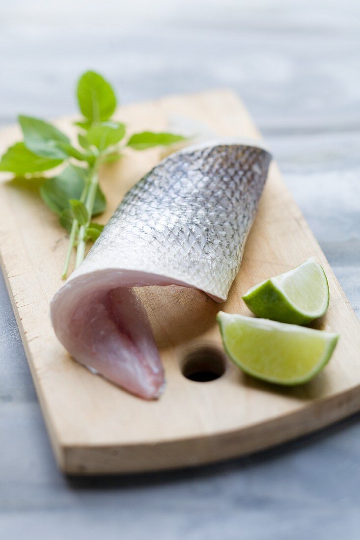 A sea bass fillet and limes on a chopping board