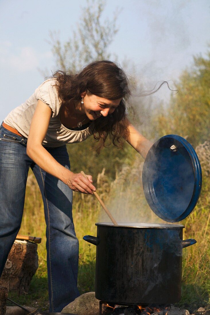 A woman stirring a large pot over an open fire