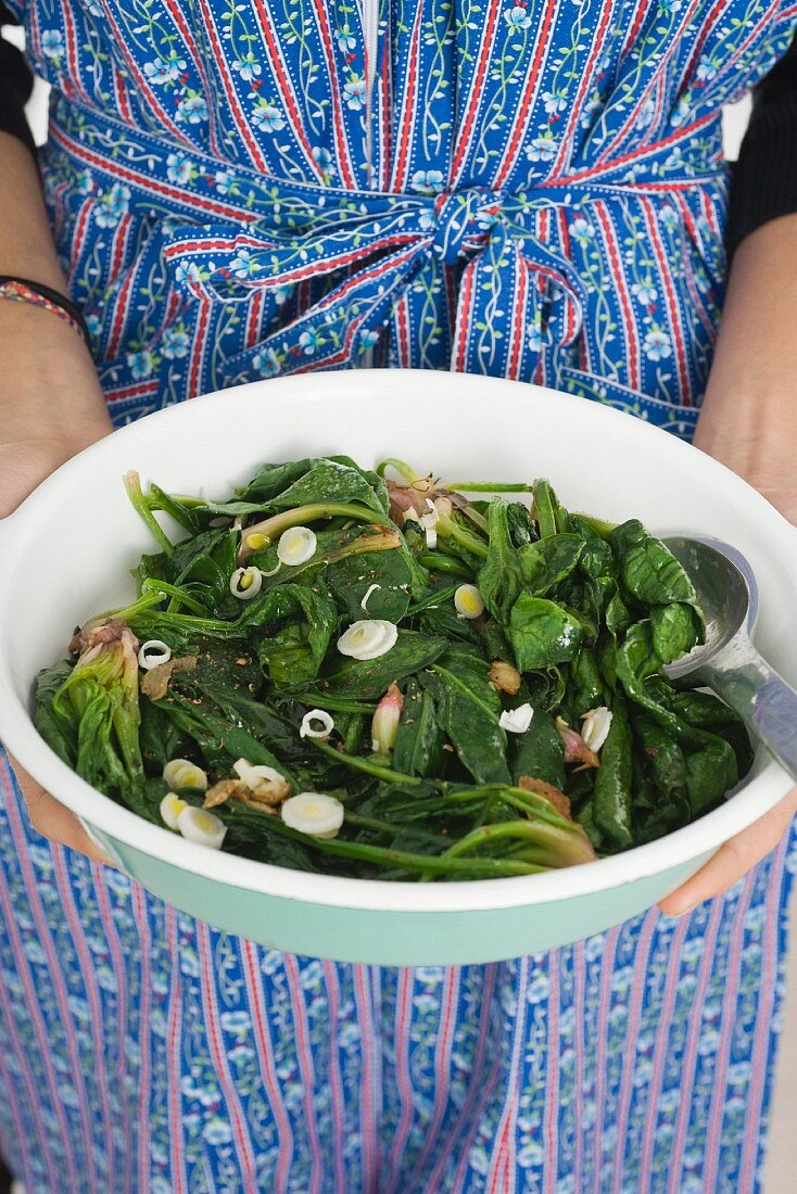 A woman holding a bowl of cooked spinach with ginger and garlic