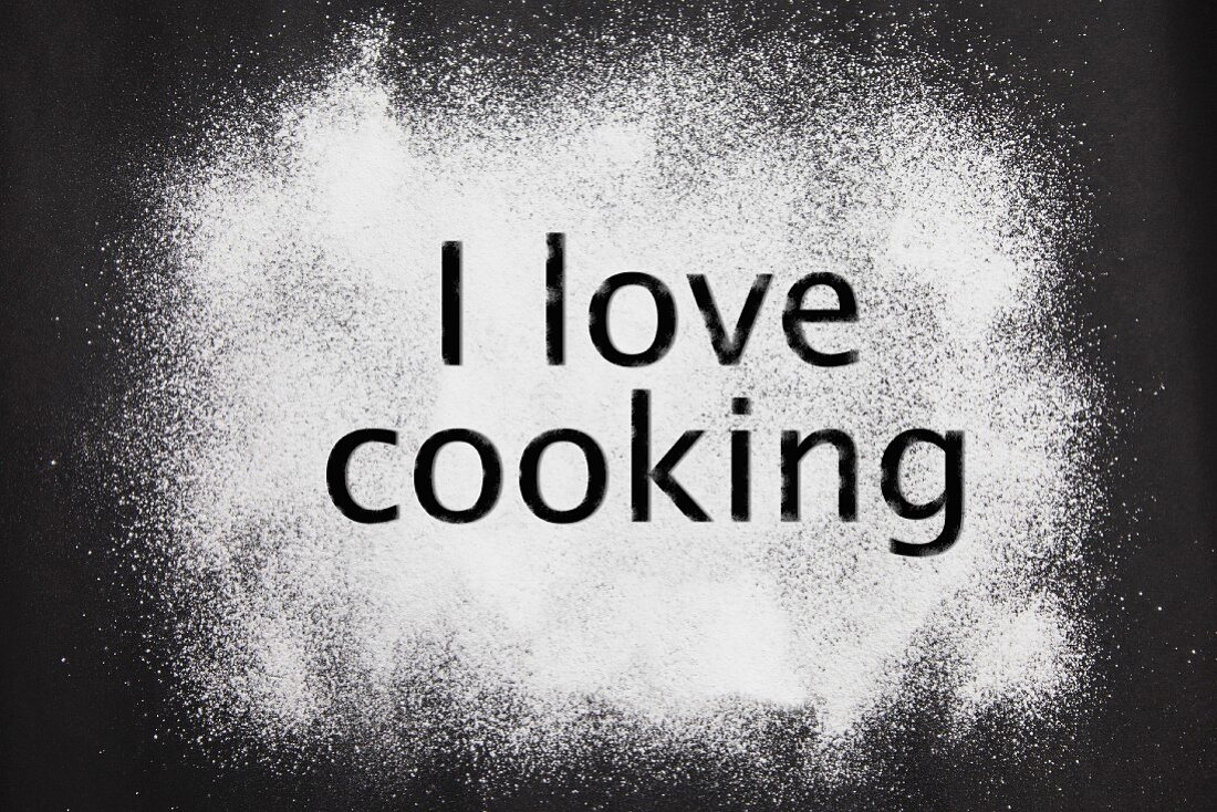 Schriftzug I love cooking in Puderzucker vor dunklem Hintergrund