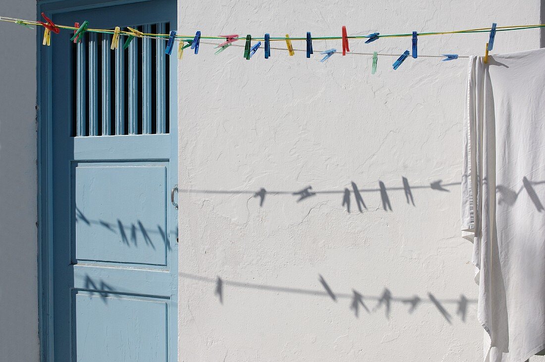 Colourful clothes pegs on washing line in front of exterior wall with pale blue wooden door