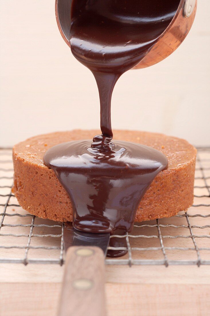 Sachertorte (rich chocolate cake from Austria) being coated with chocolate glaze