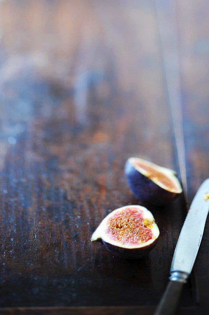 A halved fig on a wooden board with a knife