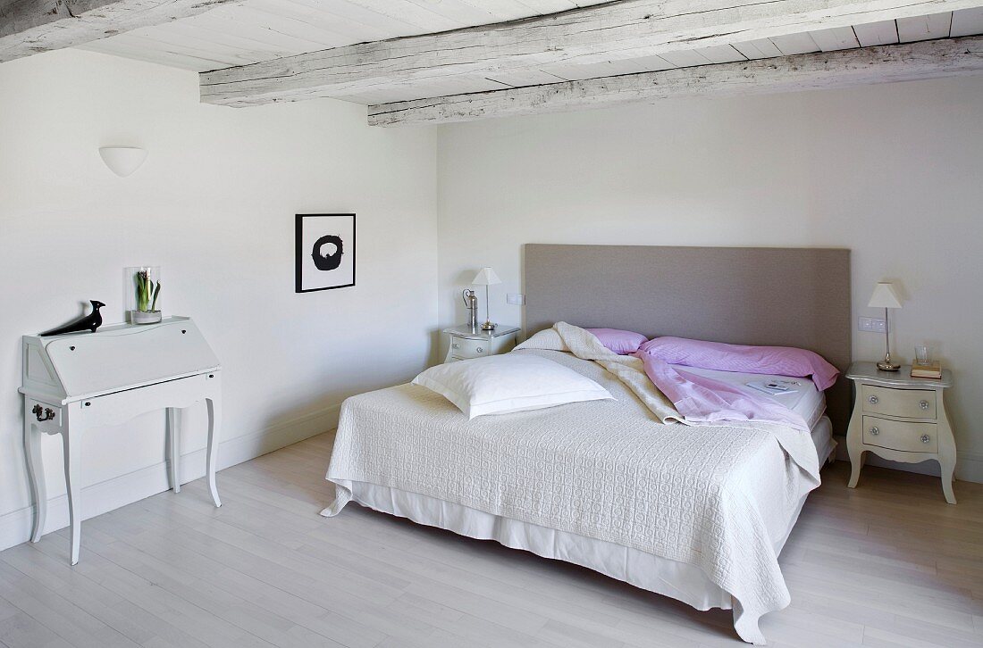 Modernes Doppelbett und traditioneller Sekretär in rustikalem Schlafzimmer mit Holzbalkendecke