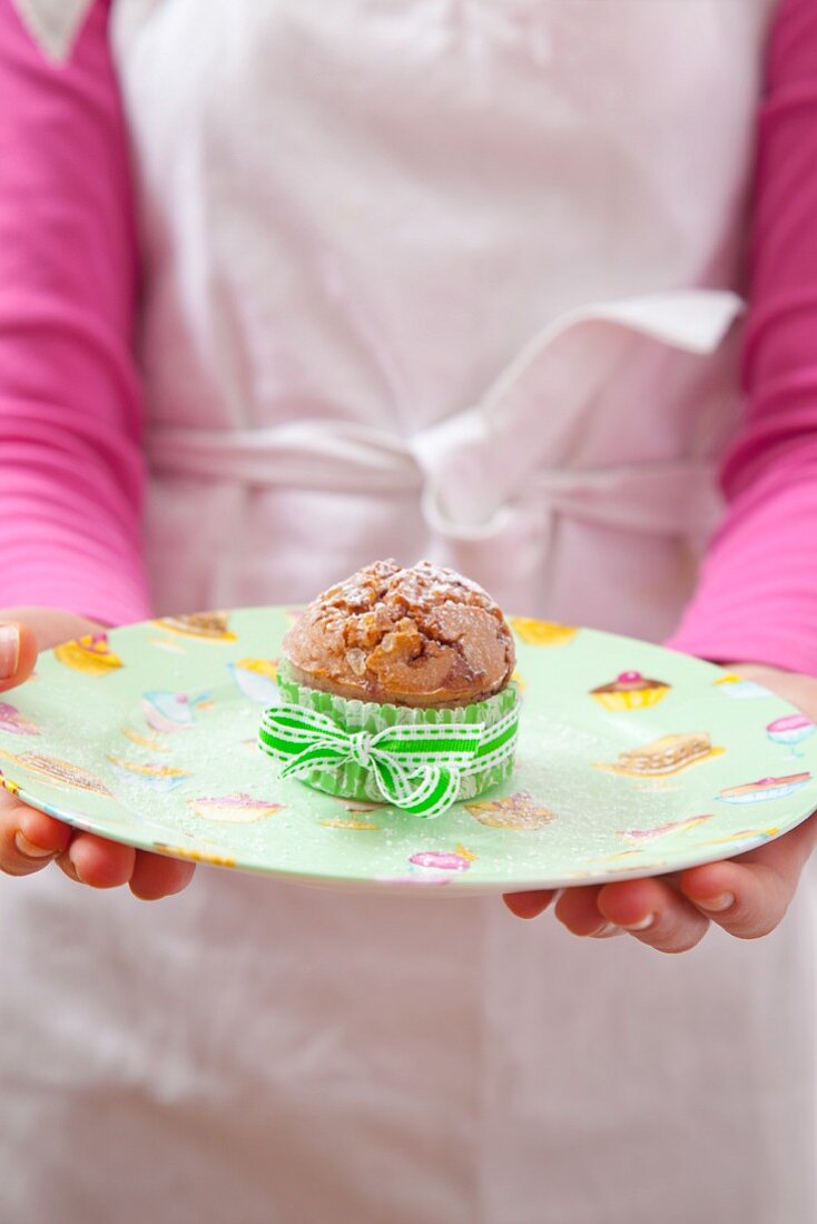 A girl holding a raspberry muffin dusted with icing sugar