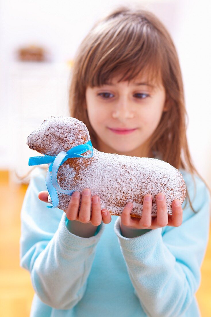 A girl holding a cake in the shape of an Easter lamb