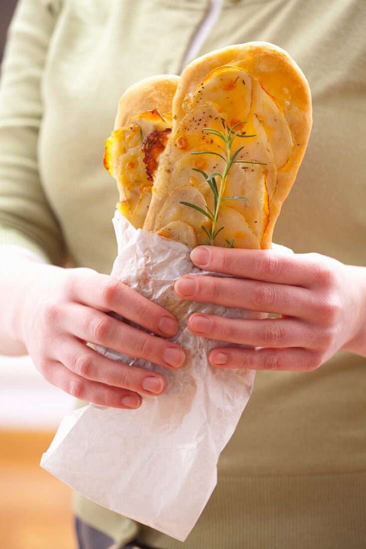 A woman holding snack-size oblong pizzas topped with potato and rosemary