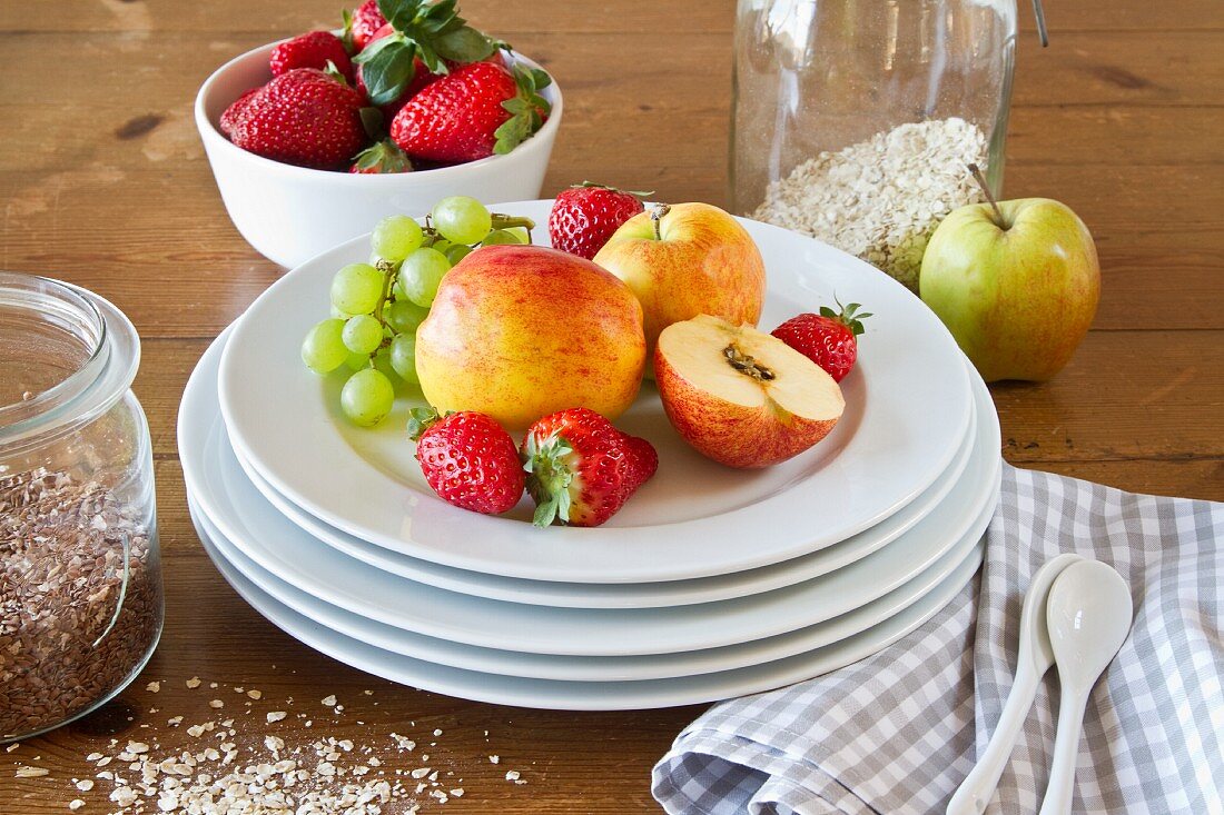 A still life featuring a stack of plates, fresh strawberries, apples and cereal grains