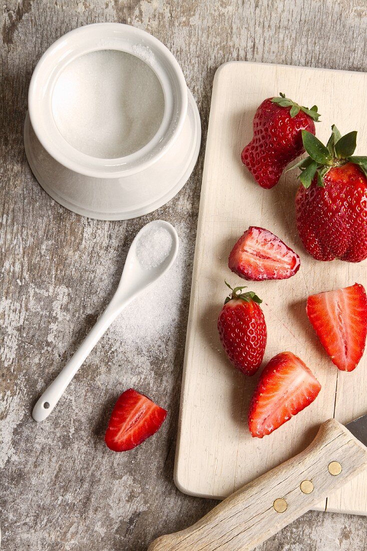 Strawberries on a chopping board; scattered sugar to one side