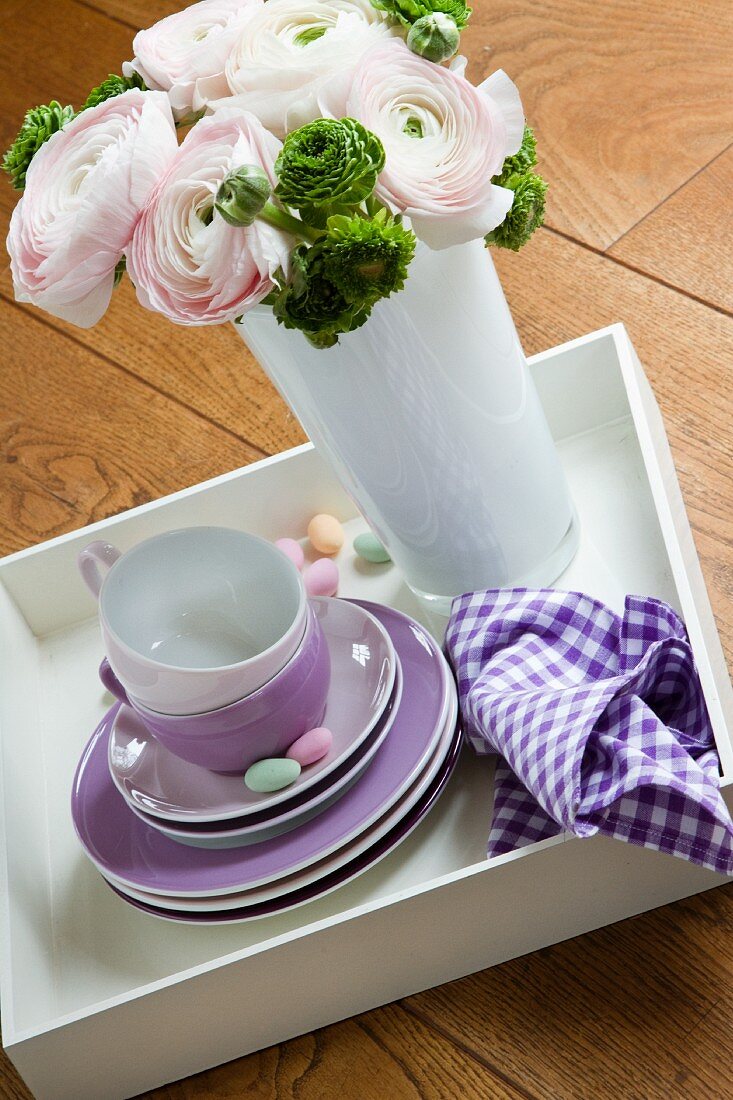 Frühlingsblumenstrauss in einer Vase neben gestapeltem Kaffeegeschirr
