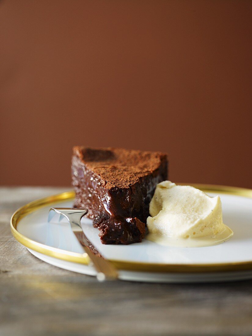A slice of chocolate cake with cocoa powder and vanilla ice cream