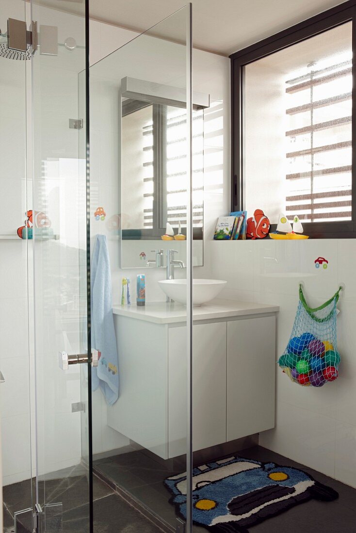 Glazed shower area next to washstand with white base cabinet in corner of bathroom below window