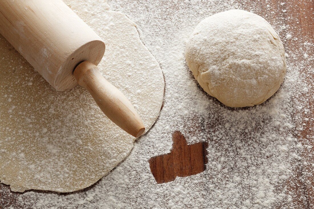 Rolled-out pastry with a rolling pin, a ball of dough, and flour with a 'like' symbol