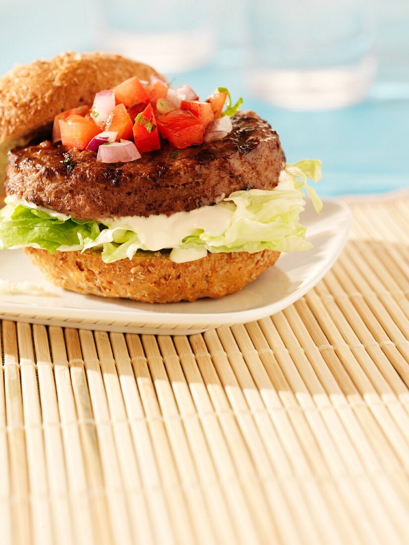 A beefburger in a bun with mayonnaise, salad and salsa