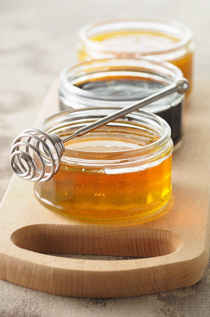 Three jars of honey on a chopping board