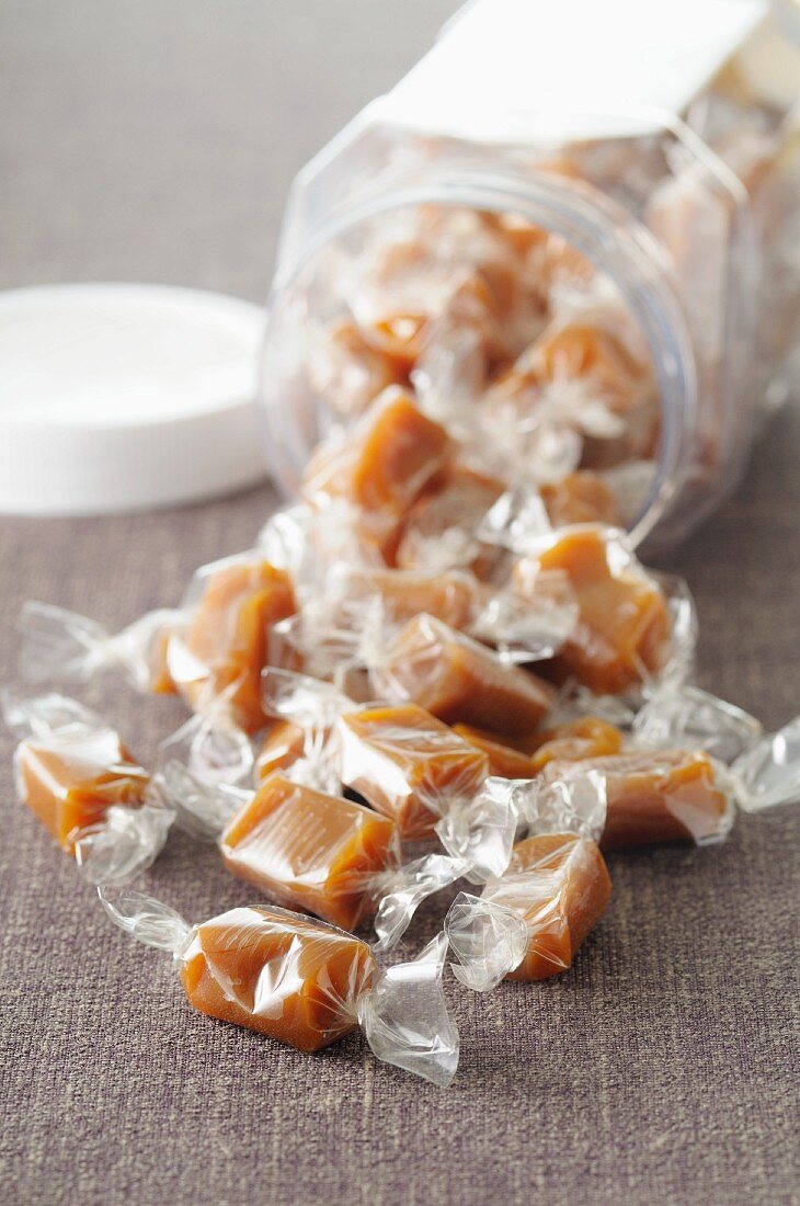 Lots of wrapped toffees in front of and inside an overturned storage jar