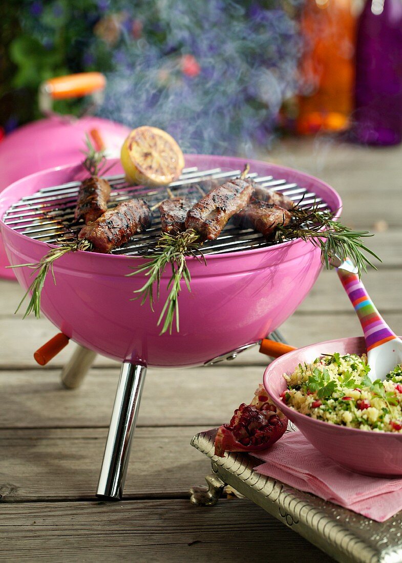 Lamb and rosemary kebabs on a pink barbecue, and tabbouleh