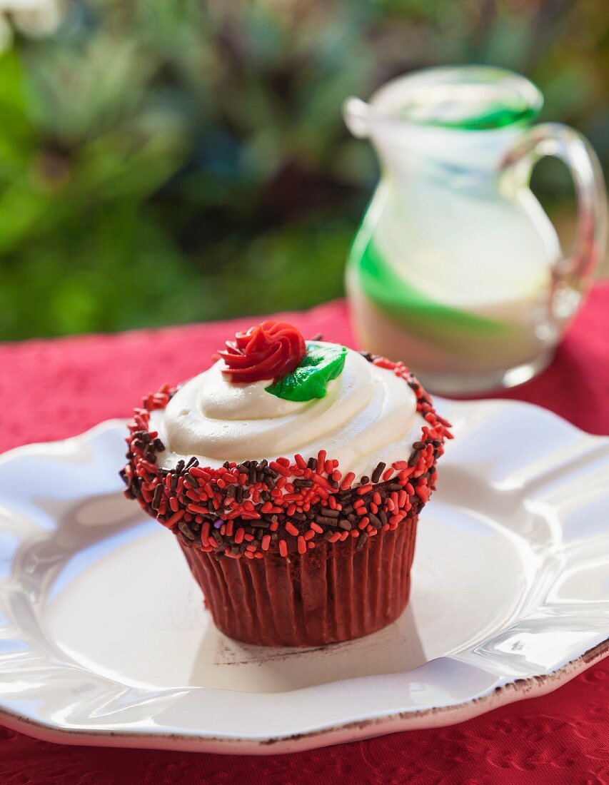 Cupcake with Vanilla Icing, Red and Chocolate Sprinkles and a Red Frosting Rose; On an Outdoor Table