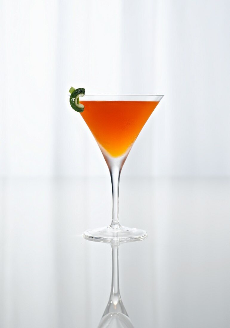 An Orange Cocktail in a Stem Glass on a Reflective Surface