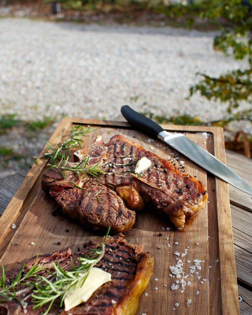 Barbecued beef steaks with butter and rosemary on a wooden board