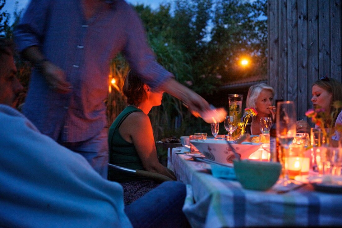 Friends sitting around a table set for a meal, outdoors in the twilight