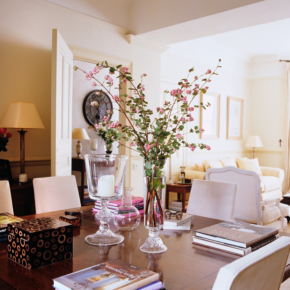 Branches of pink snowberry in vase amongst stacked books on table in traditional living room