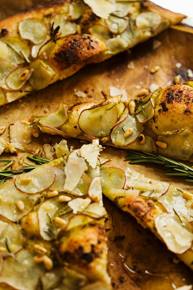 Pizzastücke mit Pesto, dünnen Kartoffelscheiben, Rosmarin und Pinienkernen