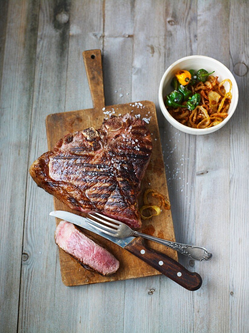 Barbecued T-bone steak with onions on a chopping board