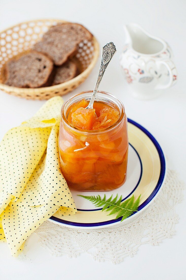 Geöffnetes Glas Melonenmarmelade mit Löffel vor Brotkorb