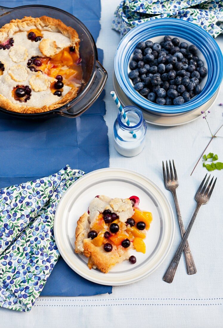 Blueberry and Peach Pie on a Plate and in Baking Dish; Bowl of Fresh Blueberries; Bottle of Milk with a Straw