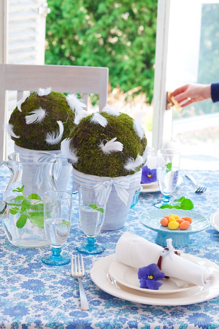 Balls of moss with white feathers in flower pots as centrepiece of Easter table