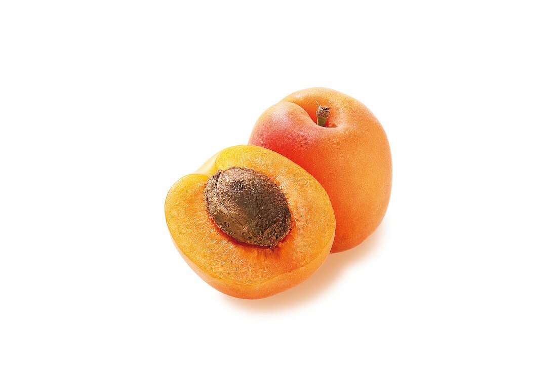 A whole and a half apricot against a white background