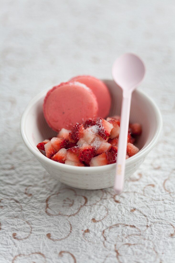 Klein geschnittene Erdbeeren mit Zucker und Erdbeer-Macarons in einer Schale