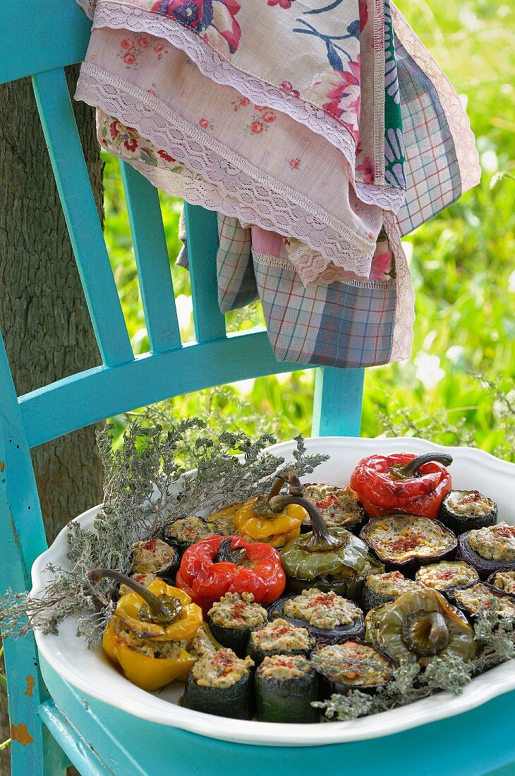 Stuffed vegetables (peppers, courgettes, onions, aubergines) on a wooden chair in the garden