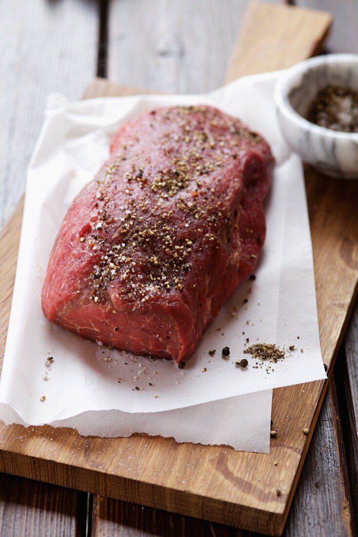 Raw sirloin of beef on paper, sprinkled with seasoning