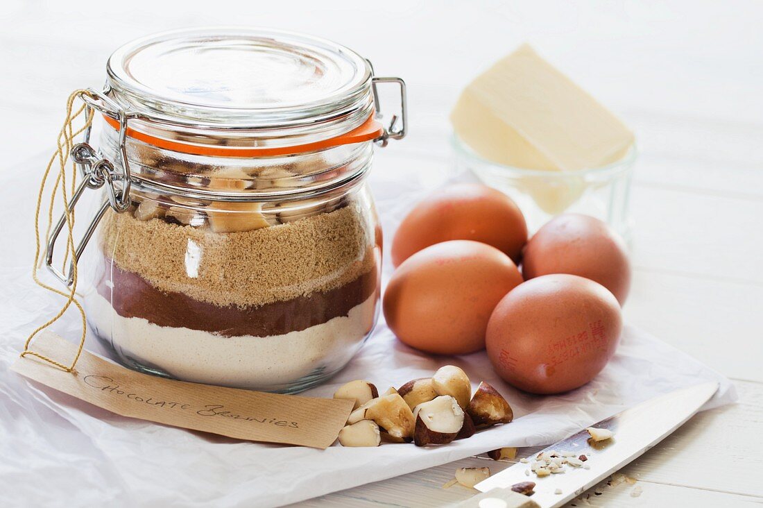 Trockene Zutaten für Brownie in einem Einmachglas, danben Eier und Butter