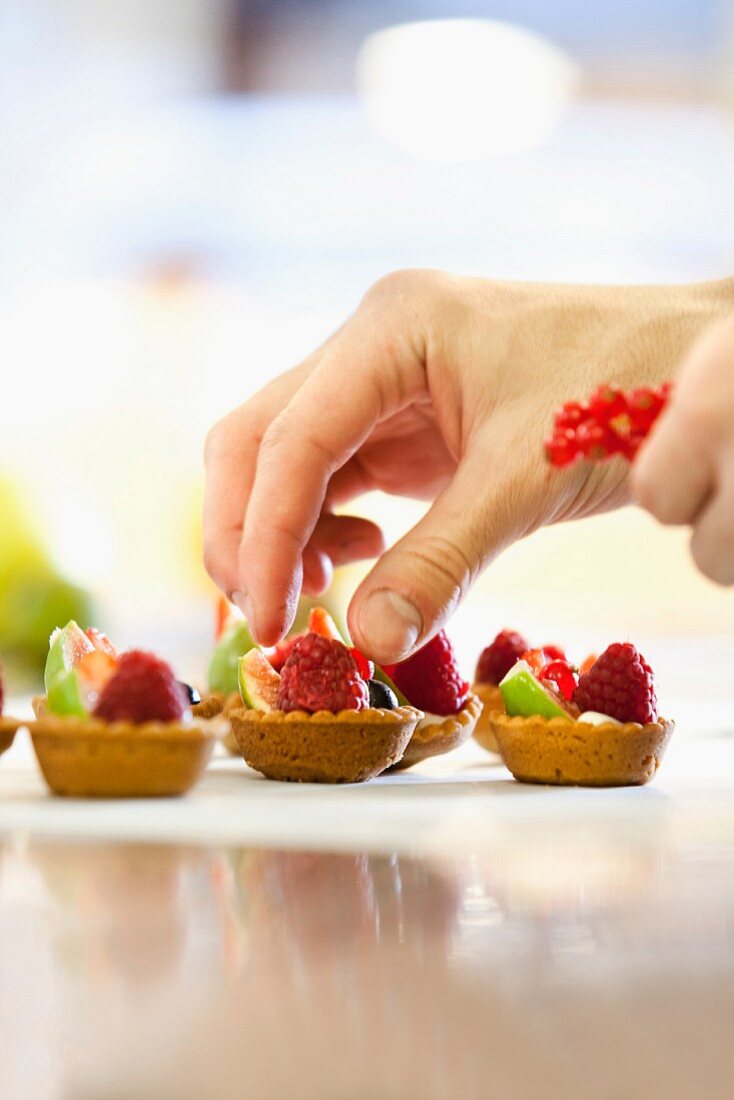 Mini tartlets being topped with fresh fruit